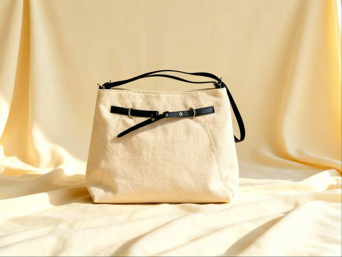 Beige cross bag with black straps on a beige fabric background