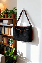 Black bag with brown strap hanging on a white wall next to a bookshelf.